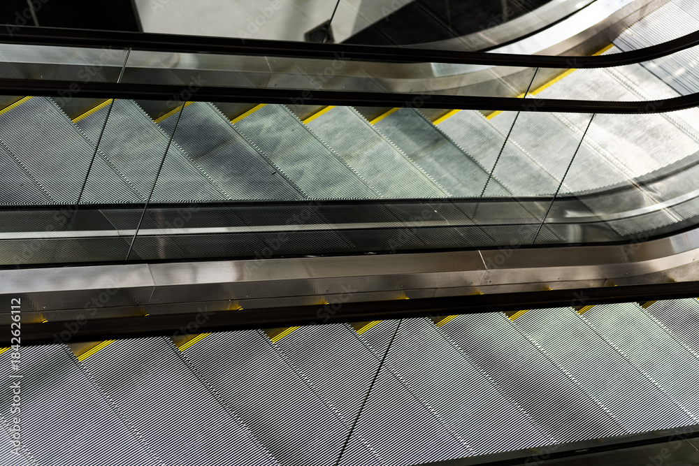 Fototapeta premium Modern Urban Architecture: Empty Commercial Escalators in Contemporary Shopping Mall Interior with Metal Railings and Glass Panels