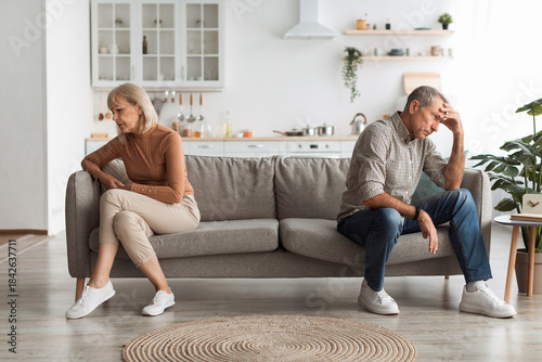 Bild auf Leinwand A couple sits apart on a sofa in a modern living room, both displaying signs of emotional distress
