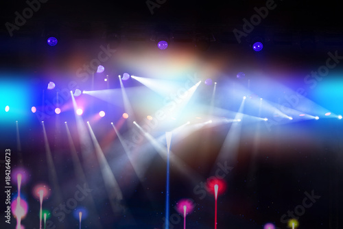 A stage with a variety of colorful lights and a spotlight. The lights are on, illuminating the stage and creating a vibrant atmosphere. The stage is dark, allowing the lights to stand out