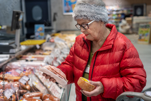 Cuadro en lienzo Senior woman reading product label while shopping for deli meat in supermarket refrigerated section