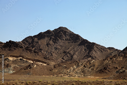 View of rugged, brown mountains rise sharply against the pale blue sky, casting shadows that accentuate their harsh, rocky texture, Quetta, Balochistan, Pakistan.