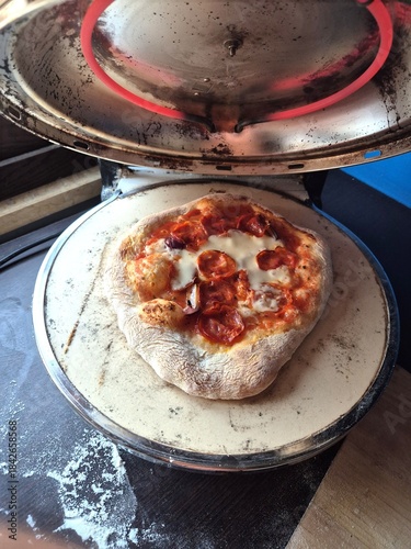 evocative image of a pizza made with spicy salami, tomato sauce, mozzarella and onions 
cooking in a home oven in Italy