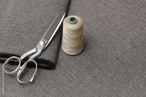 Obraz na płótnie Close-up of tailoring scissors and a spool of beige thread resting on a folded piece of gray and black wool tweed fabric with a classic herringbone pattern