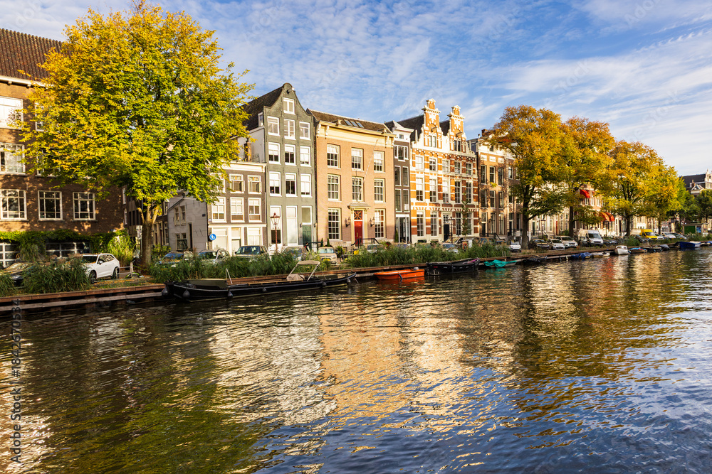 Naklejka premium Series of traditional row houses along the Singel canal seen during a golden hour afternoon, with their reflection in the water in soft focus foreground, Amsterdam, The Netherlands