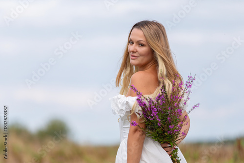 Woman in white dress holds a bouquet of wildflowers while looking back in a field during a cloudy day