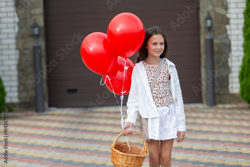 Young girl holds red balloons and a basket outside a stylish house on a sunny day