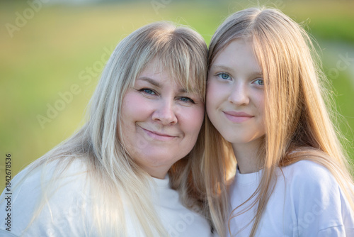 Smiling woman and girl stand close together in a sunny outdoor setting during a warm afternoon