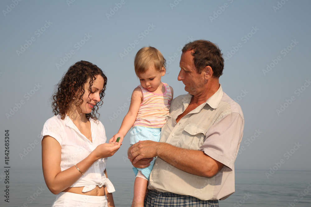 Fototapeta premium A man senior and a woman are holding a child and the woman is holding a green leaf. Scene is happy and joyful