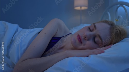 A young woman in blue pajamas relaxes and sleep on bed in the night of blue moonlight