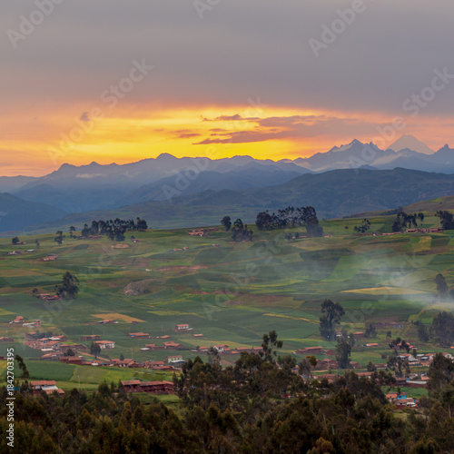 Canvastavla Chinchero, Cusco, Peru: sunset over Andean farmland with soft mist, colorful patchwork fields and distant mountains