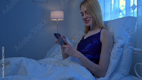 A young woman in blue pajamas relaxes before bed by using her phone in bedroom on a night with a blue moon