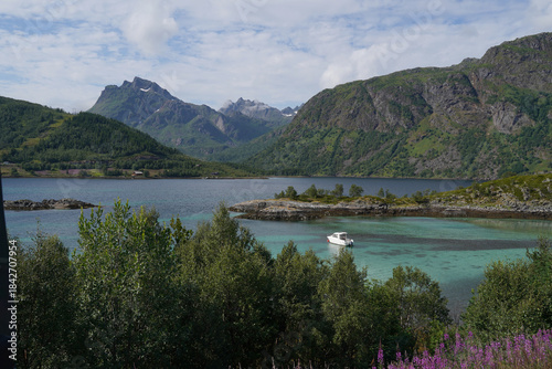 Beautiful aerial view of the harbour at Lofoten islands with green transparent water, small boat on the foreground and snowy mountains on the background.