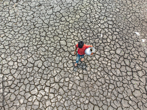 Rajshahi, Bangladesh - 09 May 2024: Aerial view of a lone figure with a water jug standing amidst the parched, cracked earth, a stark testament to drought..