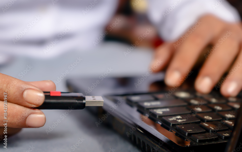 Fototapeta premium A man's hand holds a USB flash drive connected to a laptop on a table.