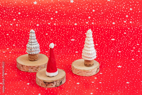 Santa hat and two knitted trees on wooden coasters on red background with copy space