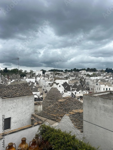 Panoramic View of Alberobello Trulli Houses with Conical Roofs and White Walls Under a Dramatic Overcast Sky, Capturing the UNESCO World Heritage Site in Puglia, Italy and European Architecture