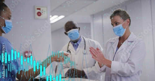 Handing nurse in blue scrubs offering device to doctor in clinic corridor, white coat, data overlay