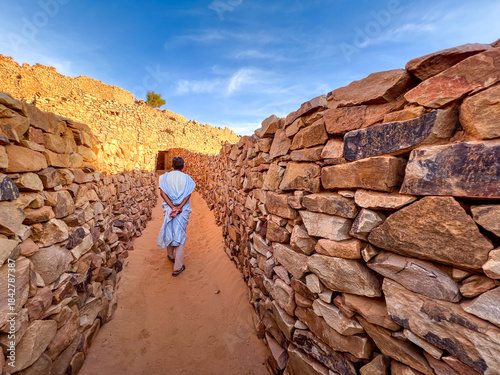 Ouadane in Mauritania. A man walks in a narrow alley of the old town between two stone walls.