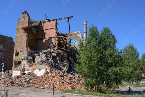 An abandoned factory with pipes, dilapidated brick buildings and pieces of walls under a clear blue sky