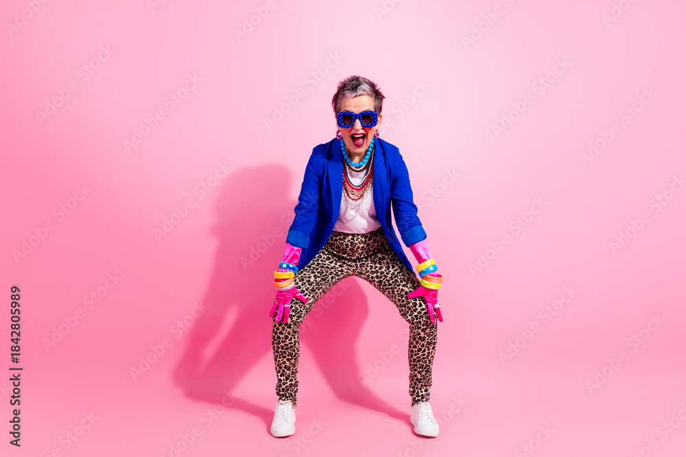 Obraz premium Vibrant retro fashion senior model in blue jacket leopard pants striking playful pose against pink background