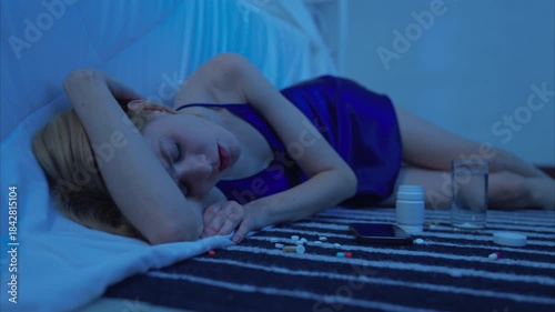 Depressed young woman lying on the floor with spilled pills, portraying mental health struggles, addiction, or emotional distress in a dark moment