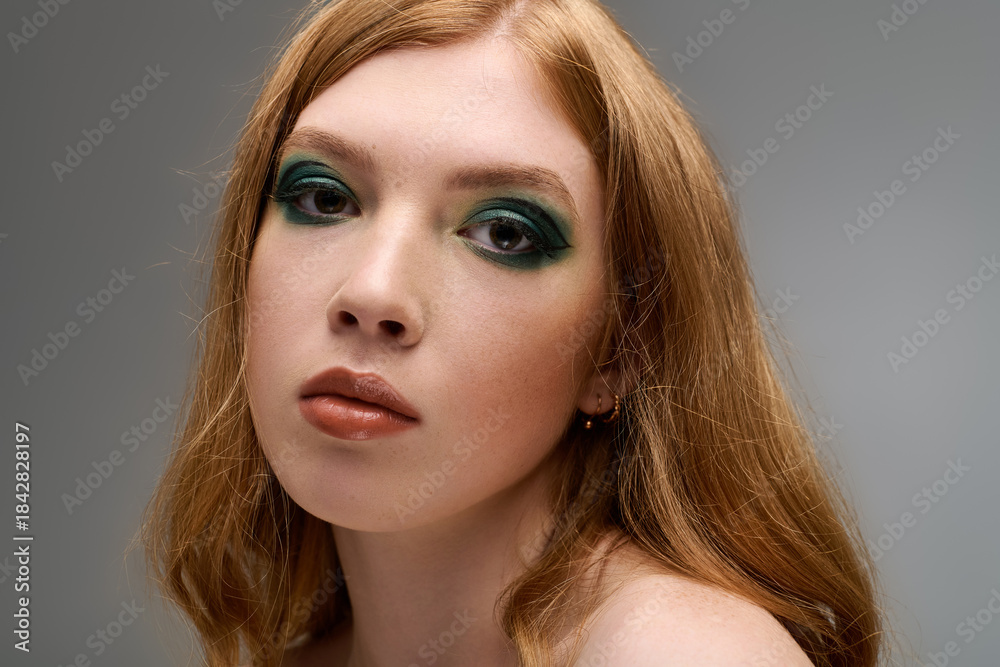 Fototapeta premium Bold makeup highlights beauty of redhead young woman in a grey studio setting
