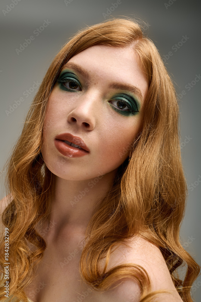 Naklejka premium Striking young woman with bold green eye makeup posing in a grey studio setting