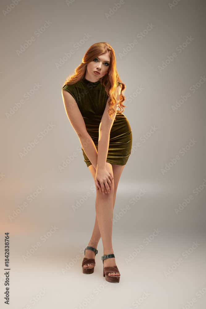 Naklejka premium Bold and stylish redhead woman poses gracefully in a grey studio setting
