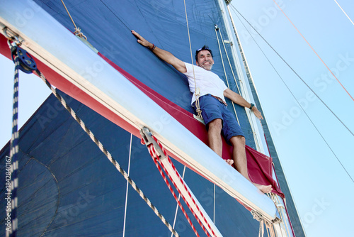 Photography experienced sailor enjoys the elevated view while standing on the boom of the ma