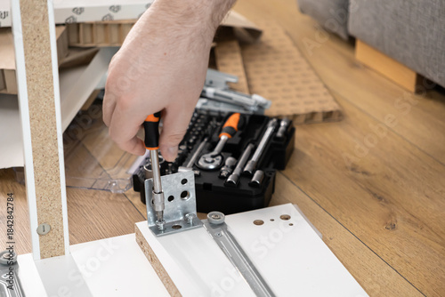 фотографія Man's hand carefully using a screwdriver to assemble new white wooden furniture,