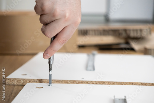 Wallpaper Mural Person's hand uses a screwdriver to assemble new flat-pack furniture, illustrating DIY home improvement, renovation, and practical skill development Torontodigital.ca
