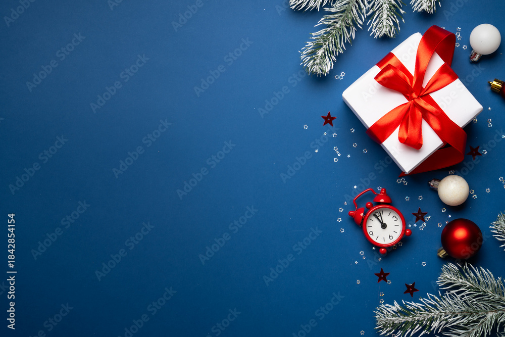 Obraz premium Christmas present box, clock, decorations and fir tree branches at blue background. Flat lay image with space for design.