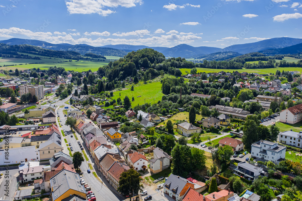 Naklejka premium Aerial drone view of Jesenik town in Czech Republic showcasing the central market square and historic buildings nestled in Jeseniky Mountains, panoramic urban landscape in sunny summer day
