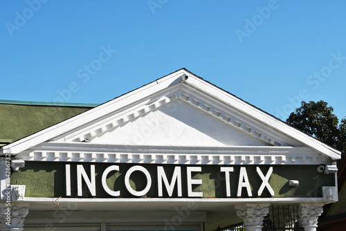 Fotografi Closeup of the words Income Tax  on a building Sign with a blue sky