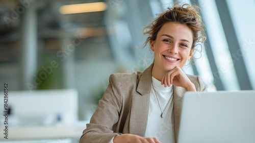 Smiling Professional at Work: A confident professional beams with a genuine smile as she works on her laptop in a modern office, embodying productivity and a positive work environment.