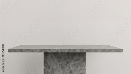 A minimalist gray table with a single pedestal base against a plain white wall background.