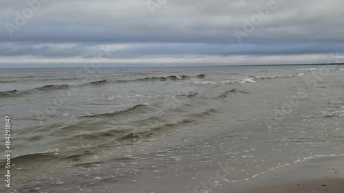 Small sea waves rolling toward the shore under an overcast sky. Calm coastal water with natural ocean ambience and real sound. Peaceful 4K seaside footage.