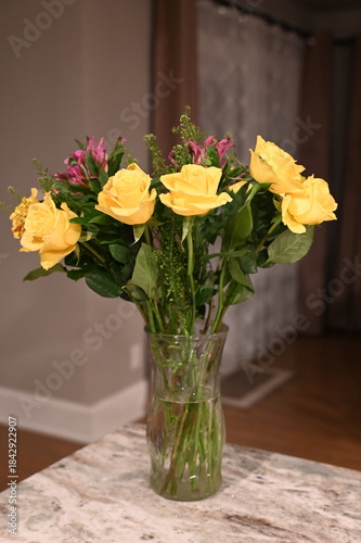 Wallpaper Mural Bouquet of fresh yellow roses and pink flowers arranged in a clear glass vase on a table, photographed indoors with warm evening light and a softly blurred home interior. Torontodigital.ca