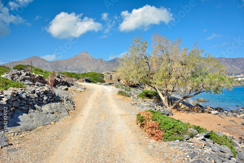 A dirt road  in Kalydon (Spinalonga) peninsula near the Elounda town in Crete, Greece. Beautiful blue sky with white clouds in the background.