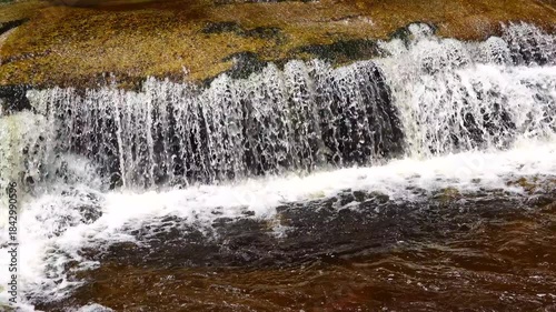 Water cascades over rocks in a river, creating splashes and ripples as it moves. natural sound