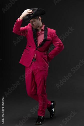 Doll-like kitsch style: man in totally pink rhinestone outfit on gray background
