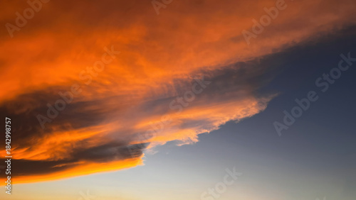Sunset clouds with a dramatic formation, reddish and bright orange in color on the horizon, blending into a soft transition toward blue-gray at the bottom left.