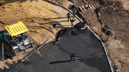 Aerial top view of road construction workers paving fresh asphalt with heavy machinery. Infrastructure development, urban construction, road repair and industrial work concept
