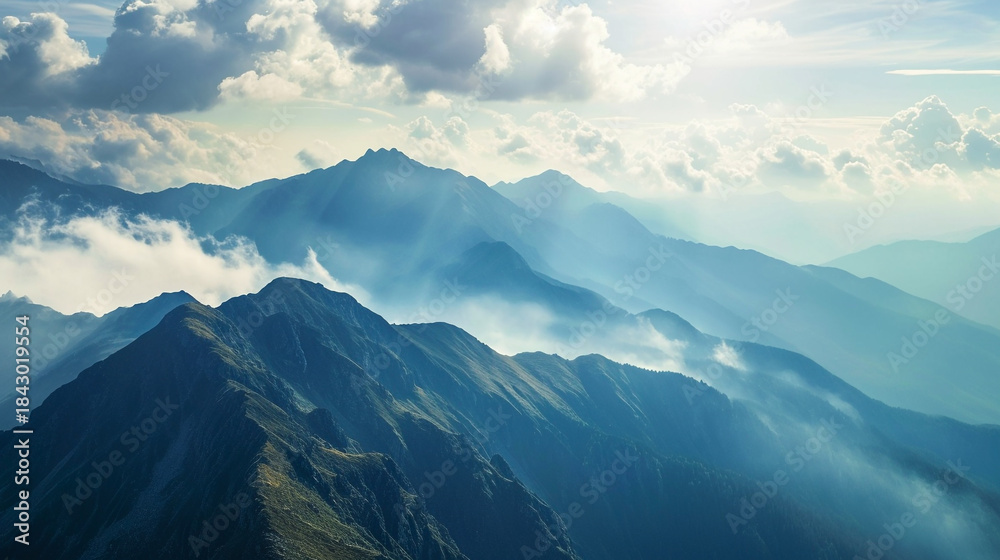 Obraz premium Majestic Mountainous Landscape with Clouds and Mist Covering Peaks and Valleys