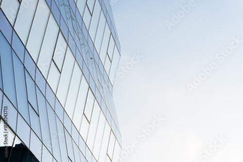 Contemporary glass office building with reflective windows and geometric lines, set against a clear blue sky. Suitable for business, architecture, and urban design concepts.