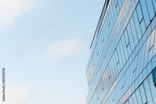 Contemporary glass office building with reflective windows and geometric lines set against a clear blue sky. Suitable for illustrating architecture, business, or urban development concepts in