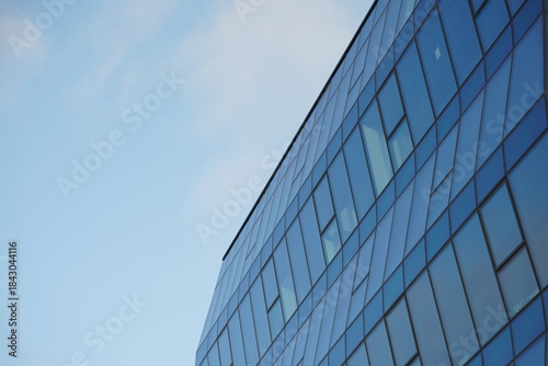 Contemporary office building with geometric glass facade reflecting the blue sky, photographed from a low angle. Suitable for illustrating architecture, business, or urban development concepts.
