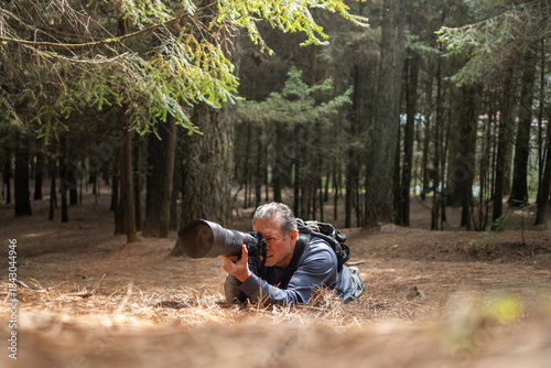 Wildlife photographer in forest lying down, capturing nature with telephoto lens