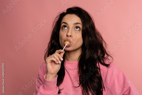 Quadro em tela Cute lady licking a yellow lollipop on the plastic stick in front of the camera