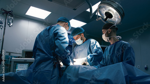 Canvas-taulu Three medical professionals, wearing blue surgical scrubs and masks, are perform